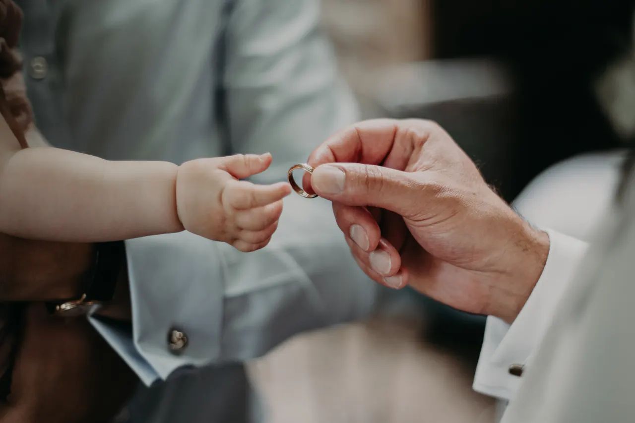 Kinderhand greift nach dem Ehering in der Hand des Bräutigams