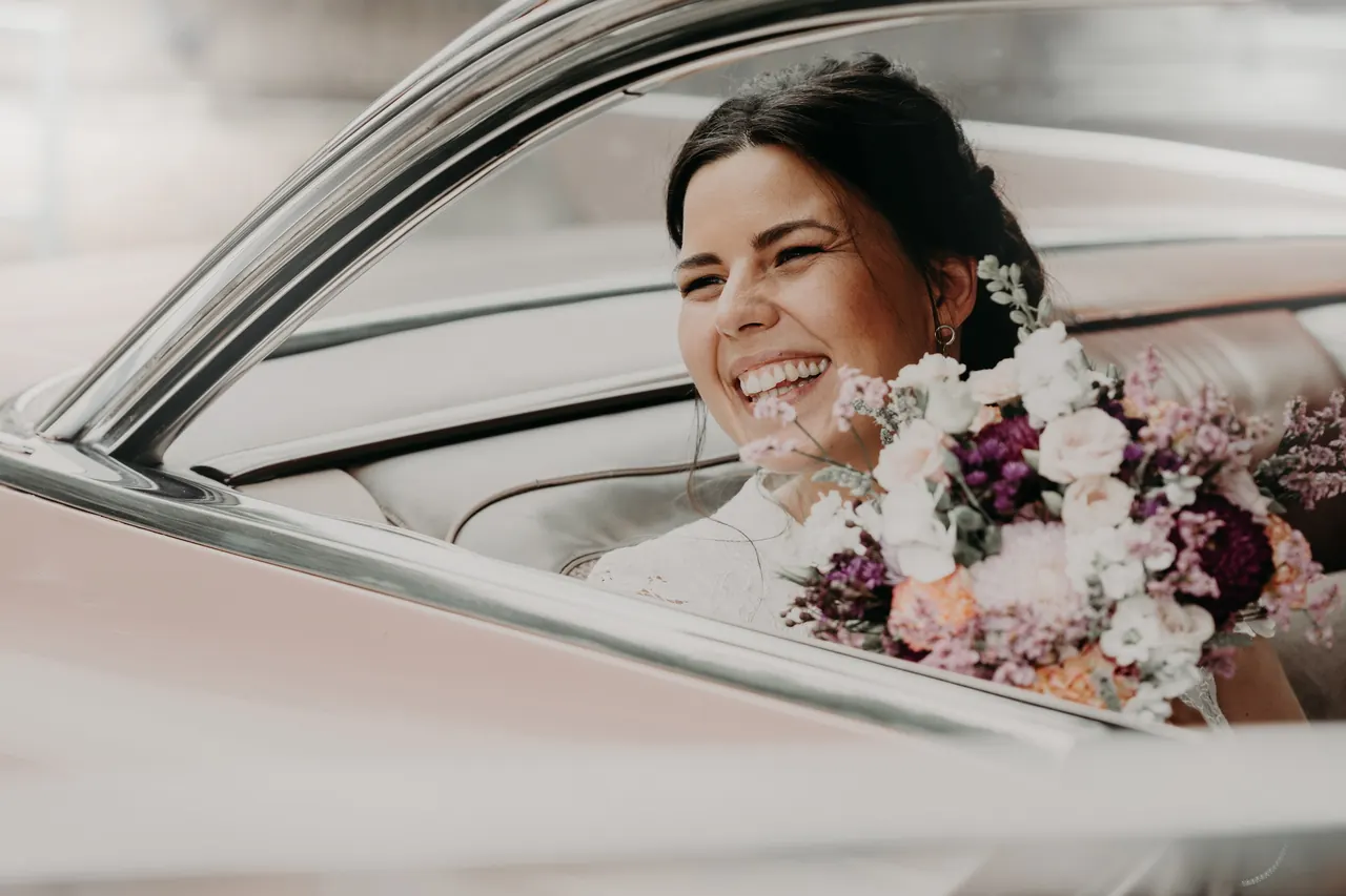Lachende Braut mit Blumenstrauß in einem Oldtimer